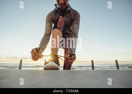 Frau schnürung Schuhe vor dem Training im Freien. Läuferin ihre Schnürsenkel binden während des Trainings an der Strandpromenade. Stockfoto