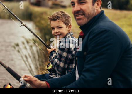 7/8 Schuß von einem Mann am Ufer eines Sees mit seinem Kind holding Angelruten. Vater und Sohn angeln tut als Freizeitbeschäftigung. Stockfoto