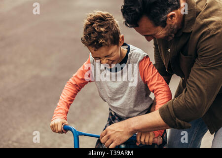 Mann, der das Fahrrad, während sein Sohn lernt es zu fahren. Junge aufgeregt, Fahrrad zu fahren. Stockfoto