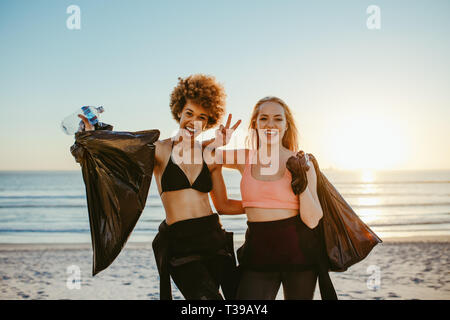 Zwei weibliche Surfer, die nach Aufnahme Wurf am Strand. Weibliche Freiwillige nach dem Reinigen der Strand, gemeinsam lächelnd und deutete vict Stockfoto