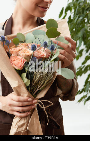 Close-up Gruß Blumen Blumenstrauß aus Rosen, frische, natürliche lebende Koralle Farbe in die Hände des Floristen Mädchen auf weißem Hintergrund mit grünen Blättern. Stockfoto