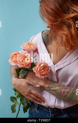 Ein Mädchen mit einem Tattoo auf der Hand zart rosa Rosen um einen blauen Hintergrund mit Platz für Text hält. Valentinstag Geschenk Stockfoto