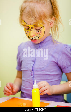 Kind Animator, der Hand des Künstlers zieht Kinderschminken zu kleines Mädchen. Kind mit lustigen Gesicht malen. Maler macht gelb Leopard am Girl's Gesicht. Childre Stockfoto