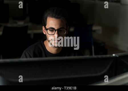 Blick über einen Bildschirm auf dem Gesicht eines jungen Informatik Schüler arbeiten mit dem Computer. Stockfoto