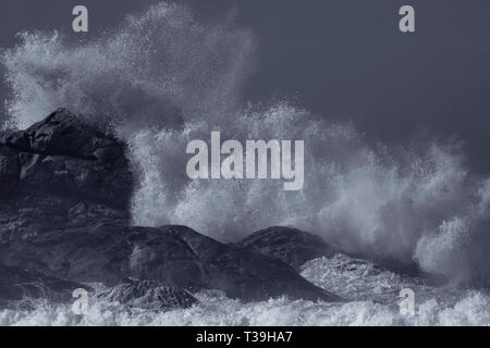 Splash von einem Brechen der grossen Meer Wellen gegen die Küste Felsen und Klippen. Umgewandelt in Schwarz und in Weiß. Farben Blau. Stockfoto