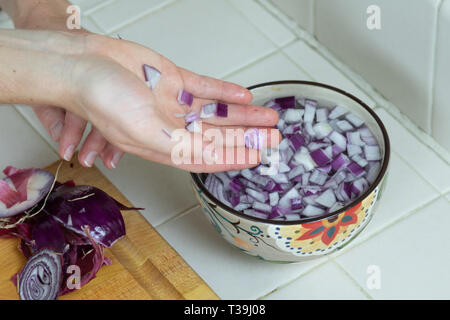 Overhead Nahaufnahme der Hand umschloss, nachdem es gewürfelte rote Zwiebel in Wasser Schüssel. Stockfoto