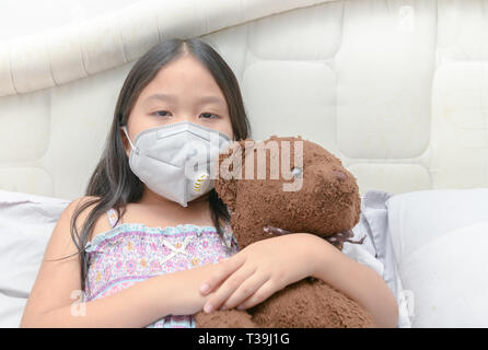 Asiatische Mädchen das Tragen einer Staubmaske PM2,5 auf dem Bett, Health Care Konzept Stockfoto