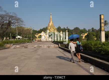 Junge paar hält einen Schirm wandern in Park & der Menschen People's Square, im Hintergrund der Shwedagon Pagode, Yangon, Myanmar (Birma) Stockfoto