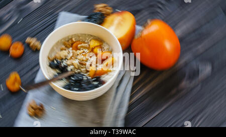 Blur in Motion Zusammenfassung Hintergrund der Haferflocken mit Kaki, Dörrpflaumen, getrocknete Aprikosen, Walnuss und Sesam auf einem schwarzen Holztisch. Stockfoto