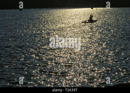 Eine einsame Person in einem Kajak Polsterung in den Sonnenuntergang über der Bucht. Stockfoto