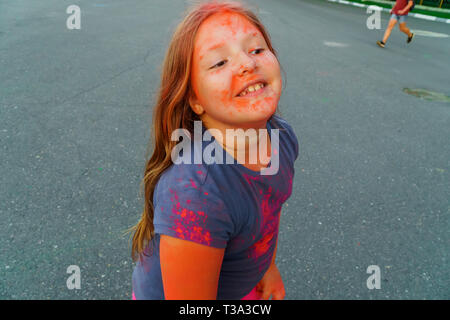 Fröhliche kleine Mädchen mit langen Haaren bedeckte Rosa und Lila trocken Farbe Holi Stockfoto