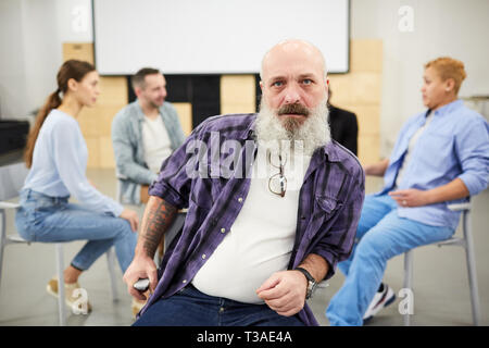 Portrait von bärtigen älteren Mann an der Kamera schaut beim Sitzen im Stuhl vor der Therapie Gruppe, kopieren Raum Stockfoto