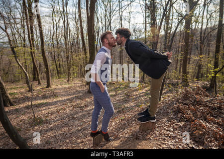 Zwei Männer, junge homosexuelle Paar schiefen, etwa zu küssen, von Angesicht zu Angesicht, während sie draußen in der Natur Park oder Wald. Stockfoto