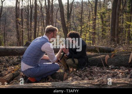 Zwei Männer, ein schwules Paar, Kuscheln mit Hund Welpen. Draußen im Wald, Freizeit. Stockfoto