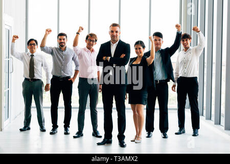 Fröhliche multiethnischen Kollegen Lächeln und die Fäuste, während in der Nähe von zuversichtlich Boss stehen und Erfolge feiern in der Nähe der Fenster im Büro Stockfoto
