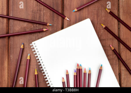 Ein Foto von einem shetchbook mit vielen verschiedenen Farbstifte um ihn herum, geschossen von oben auf einem dunklen Hintergrund mit einem Platz für Text Stockfoto