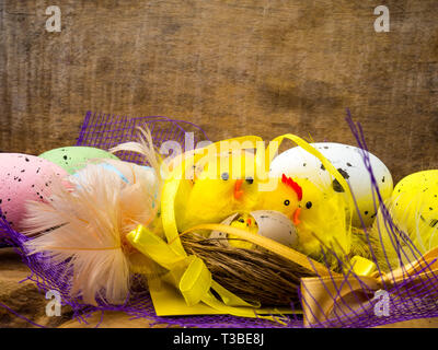 Ostern dekorative Komposition mit Nest, Farbe gelb Hühner Eier und bunten Federn auf Holzbrett. Platz kopieren Stockfoto