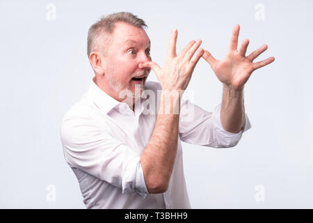 Cute älterer Mann im weißen T-Shirt teasing jemand. Studio gedreht. Positive facial Emotion Stockfoto