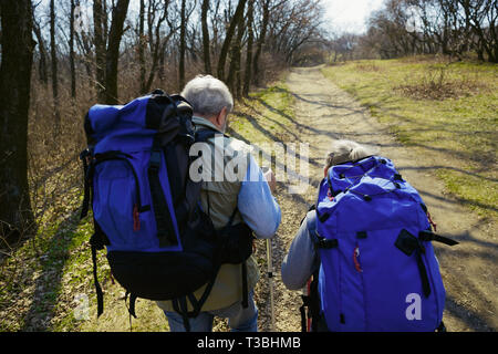 Bereit für mehr wieder. Im Alter von Familie Paare von Mann und Frau in touristische Outfit zu Fuß am grünen Rasen in der Nähe von Bäumen im sonnigen Tag. Konzept der Tourismus, gesunder Lebensstil, Entspannung und Zweisamkeit. Stockfoto