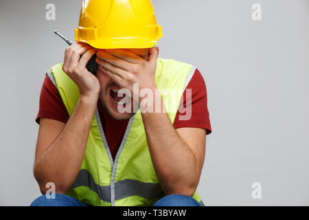 Foto von umgekippt Arbeiter Mann im gelben Helm mit Walkie talkie auf leeren grauen Hintergrund Stockfoto