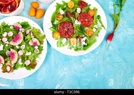 Mix Salate auf blauem Hintergrund. Frischem Zitrus Salat mit Rucola Feta, Chia, kumquat und Blut orange. Wassermelone Rettich Salat. Vegetarische, sauber Essen Stockfoto