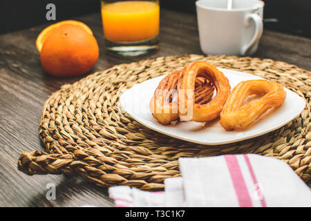 Leckere spanische Churros, Orangensaft, Kaffee Frühstück. Orange in Scheiben geschnitten. Tischplatte mit Churros. Im Sommer Frühstück Stockfoto