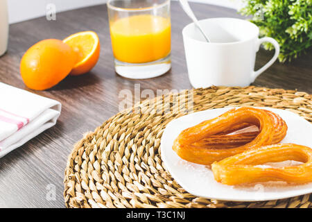 Leckere spanische Churros, Orangensaft, Kaffee Frühstück. Orange in Scheiben geschnitten. Tischplatte mit Churros. Stockfoto