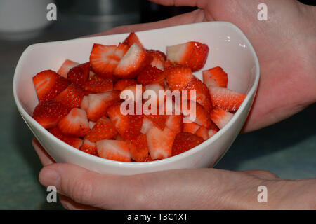 Gepflegte frau Hände halten ein weißer Keramik Keramik Schüssel mit frisch geschnittenen Erdbeeren, süß und Rot schneiden Erdbeeren in einem Keramik Keramik Stockfoto