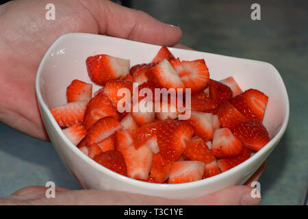 Der reife rote und süße schneiden Erdbeeren in einem Keramik Töpferei schließen, gepflegte Frau Hände halten ein weißer Keramik Keramik Schüssel mit frisch Stockfoto