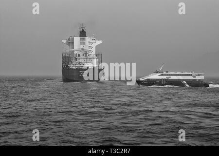 Schwarz-weiß Foto des Containerschiffes, BINDIIPSA, verlassen den Osten Lamma Kanal, Hong Kong. Eine schnelle Fähre an den Stern. Stockfoto