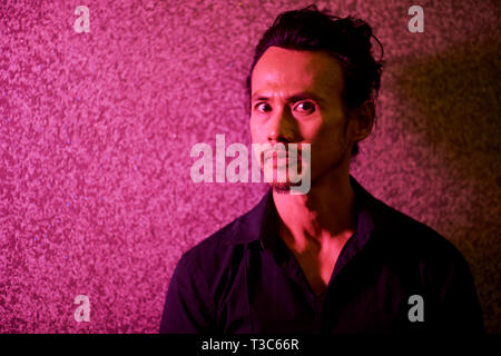 Portrait von Asiatischen jungen Mann gegen die Wand und Kamera mit ernsten Blick Stockfoto