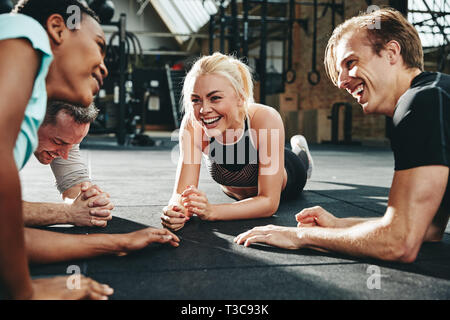 Vielfältige Gruppe von lachenden Menschen in Sportswear liegen zusammen auf einen Fitnessraum, eine Pause von Ihren Workout Stockfoto