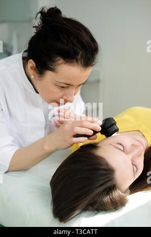 Weibliche Dermatologe mit einem professionellen Dermatoskop beim Tun der Haut Untersuchung, Kontrolle gutartige Muttermale im Gesicht. Dermatologe Muttermal untersuchen Stockfoto