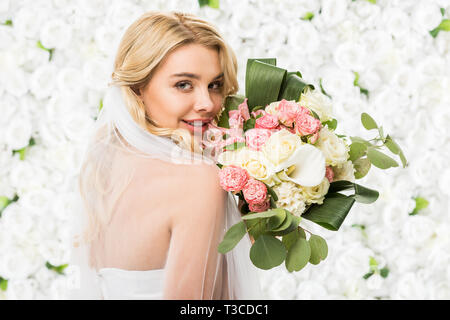 Lächelnd attraktive Braut Holding wedding bouquet auf weißem floral background Stockfoto