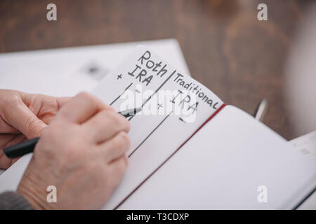 7/8-Ansicht der älteren Frau schreiben in Notebook mit Roth IRA und traditionelle ira Worte Stockfoto