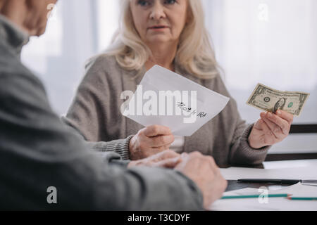 7/8-Ansicht von Senior Paar hält Umschlag mit "Roth IRA" Schriftzug und Dollar Banknote Stockfoto
