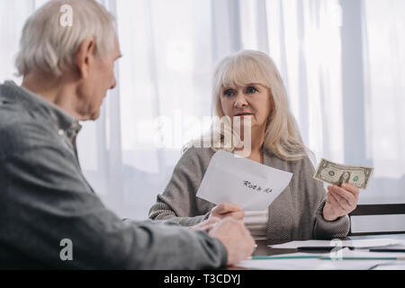 Senior Paar hält Umschlag mit "Roth IRA" Schriftzug und Dollar Banknote zu Hause Stockfoto