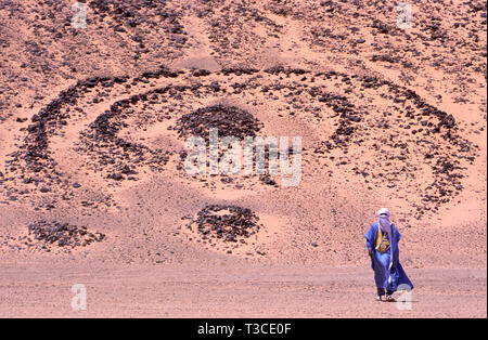 Tuareg Mann in einer Tracht mit einem 5000 Jahre alten Grab im Hintergrund in der Sahara in Algerien Stockfoto