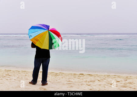Mann mit bunten Regenschirm an einem Sandstrand in Malediven Stockfoto