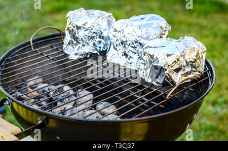 Baby Back Ribs Krone Braten auf BBQ Grill Kugelgrill. Hausgemachte Schweinerippchen auf einem Grill mit geringe und langsame Methode. Rippen eingewickelt in Alufolie, die Stockfoto
