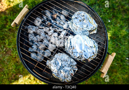 Baby Back Ribs Krone Braten auf BBQ Grill Kugelgrill. Hausgemachte Schweinerippchen auf einem Grill mit geringe und langsame Methode. Rippen eingewickelt in Alufolie, die Stockfoto