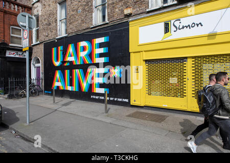 Zwei Männer hinter Graffiti in Dublin' U sind Lebendig" Stockfoto