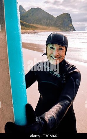 Eine glückliche Frau mittleren Alters Surfer in einem Neoprenanzug an Unstad Arktis surfen weltweit die am nördlichen arktischen Surf resort Strand von Unstad auf den Lofoten norwegen Stockfoto