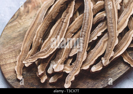 Scheiben getrocknet Lingzhi mushroom, auch genannt oder Reishi Ganoderma Lucidum, auf einem Holzbrett, grauen Hintergrund. Traditionelle chinesische Medizin Produkt. Stockfoto