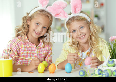 Cute zwei Schwestern tragen die Hasenohren und Malerei Ostereier Stockfoto