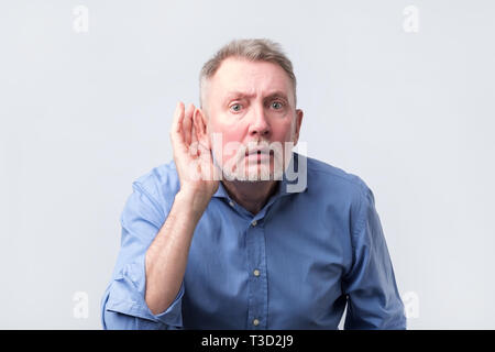 Älterer Mann im blauen Hemd leiden unter Schwerhörigkeit. Er will frische Gerüchte zu hören. Stockfoto