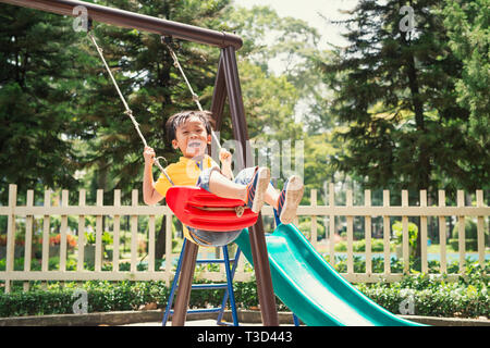 Freudige Junge im Grundschulalter reiten Spielzeug auf Kinderspielplatz Stockfoto