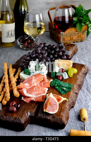 Gerichte für einen Snack Antipasti auf einem Holzbrett mit Prosciutto, verschiedene Käse, Trauben und Feigen auf einem Tisch mit Wein Stockfoto