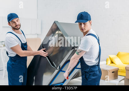 Zwei movers in Uniform mit hand-Lkw während des Transports Kühlschrank im Apartment Stockfoto