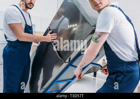 7/8-Ansicht von zwei movers mit hand-Lkw während des Transports Kühlschrank im Apartment Stockfoto